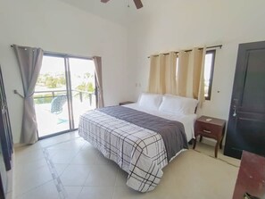 Een slaapkamer met een bed, nachtkastje, raam met gordijnen en een deur.