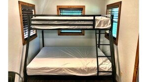 A bunk bed room with two windows, each with blinds, and a small window above the bed.