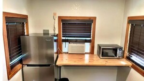 A compact kitchenette with a stainless steel refrigerator, a microwave, and a wooden countertop.