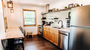 Una cocina con armarios de madera, un refrigerador de acero inoxidable, una mesa de comedor con sillas y una ventana con persianas.