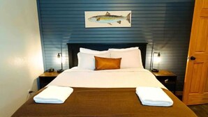 Una habitación de hotel con una cama, una manta marrón, almohadas blancas y un cuadro de un pez en la pared.