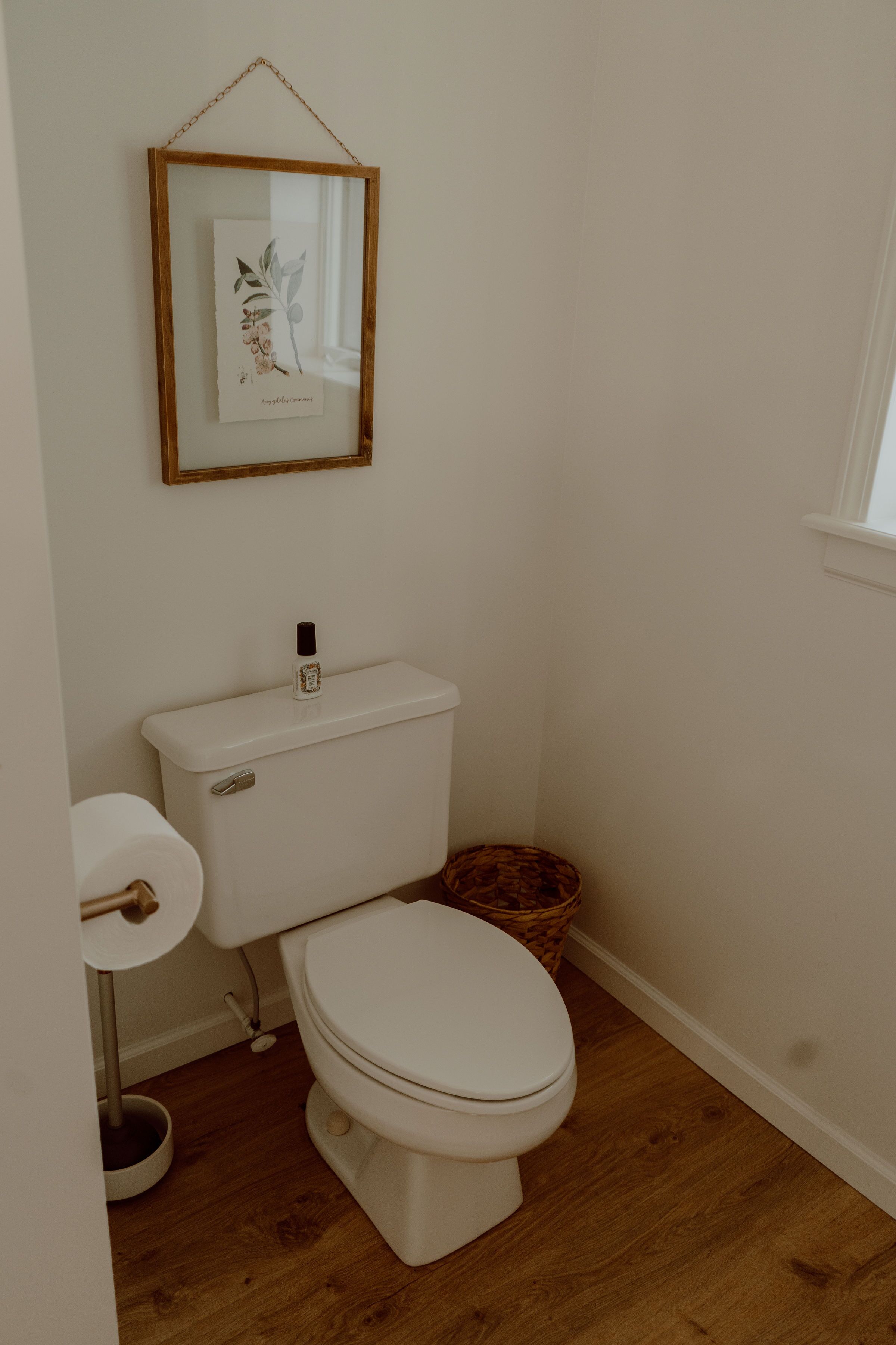A bathroom with a toilet, a bidet, a wooden floor, and a framed picture on the wall.
