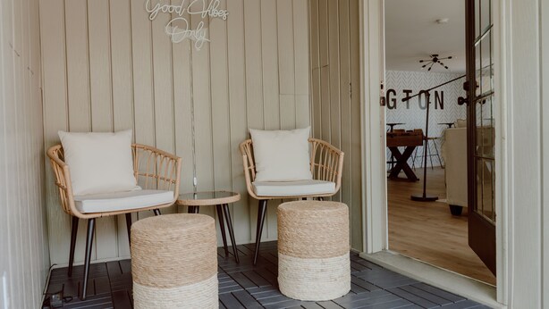 A cozy seating area with wicker chairs and ottomans, a small round table, and a decorative sign.