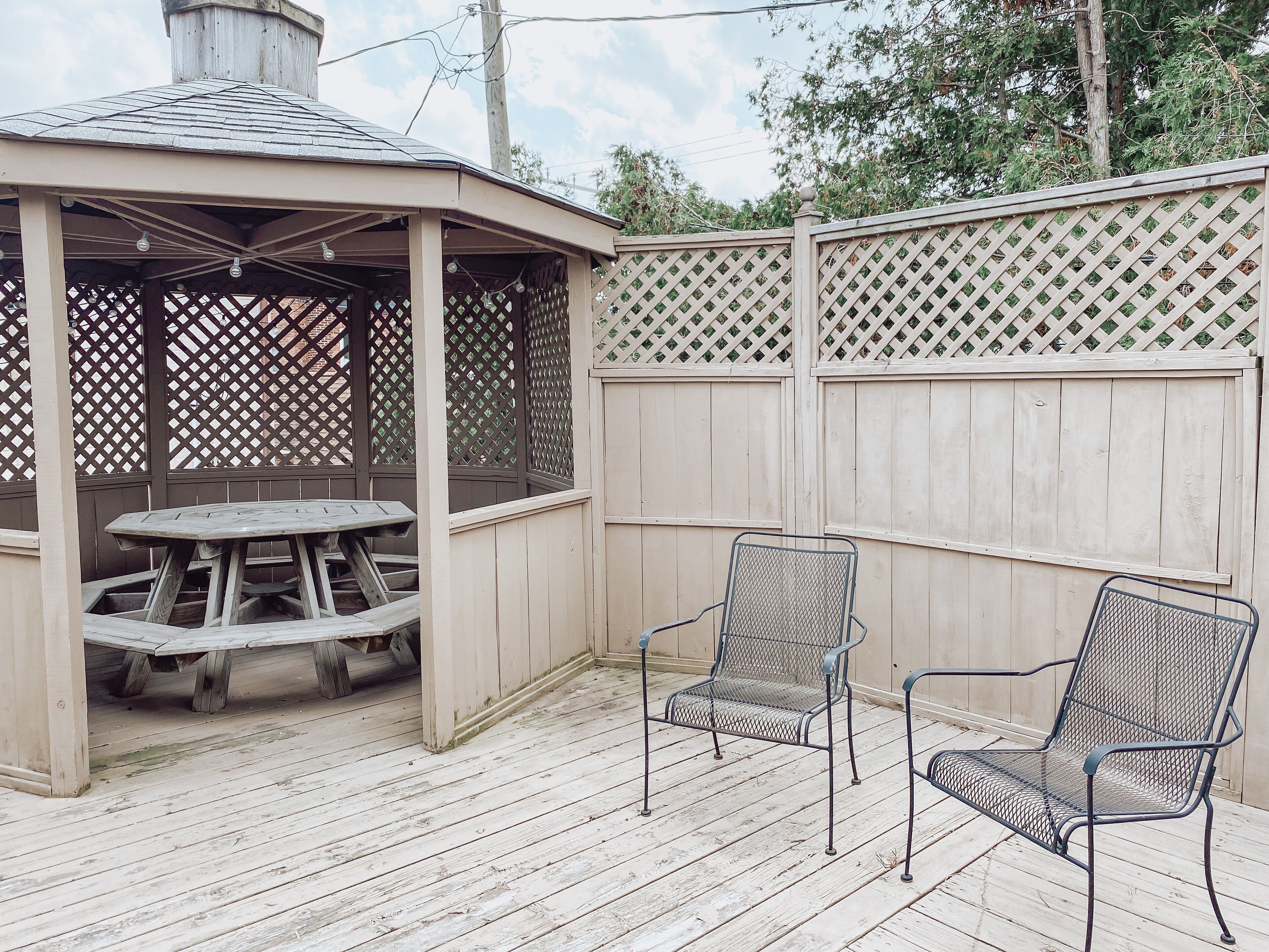 A wooden deck with a covered seating area, a picnic table, and two metal chairs.
