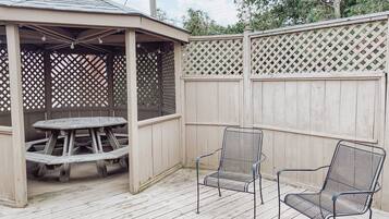 A wooden deck with a covered seating area, a picnic table, and two metal chairs.