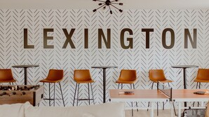 A room with a herringbone patterned wall, a large 'LEXINGTON' sign, and a seating area with tables and chairs.
