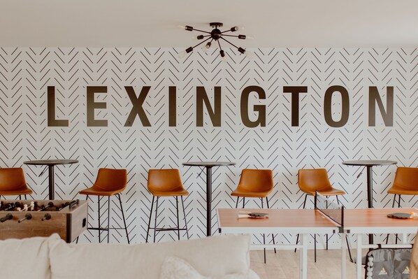 A room with a herringbone patterned wall, a large 'LEXINGTON' sign, and a seating area with tables and chairs. - The Main Hen House, trendy downtown Main St location, walk to everything! (Lexington)