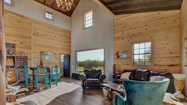 Un vaste salon aux murs en bois, doté d’une grande fenêtre, d’un canapé en cuir et d’un coin repas avec des chaises turquoise.