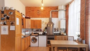 A compact kitchen with wooden cabinets, a built-in washing machine, a stove, and a dining area with a wooden table and chairs. - Apartment 74 (Nottingham)