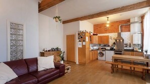 A cozy living room with a leather sofa and a dining table, connected to a kitchen with wooden cabinets and a brick wall. - Apartment 74 (Nottingham)