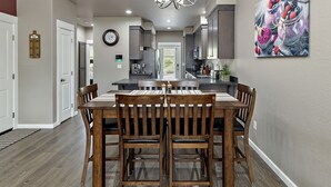 A modern kitchen with dark cabinets, a central island, and a dining area with wooden chairs and a bench. - Galaxy-Themed, Fastest WiFi, 3 King Beds Home (Medford)