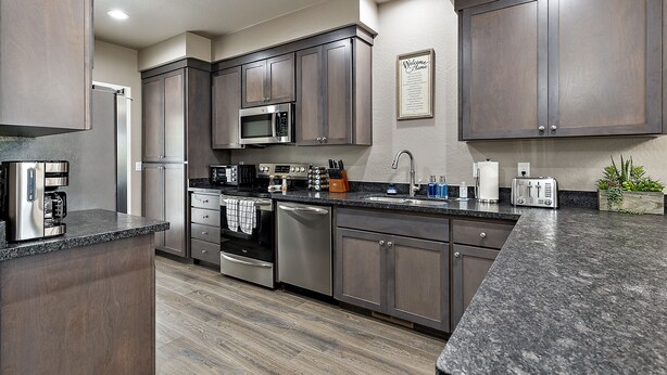 A modern kitchen with dark wood cabinets, stainless steel appliances, and a granite countertop. - Galaxy-Themed, Fastest WiFi, 3 King Beds Home (Medford)