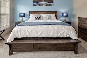 Una cama con cabecero de madera, dos mesitas de noche con lámparas, y una pared azul con un cuadro de la Tierra.