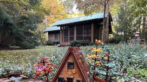 Una cabaña de madera con techo de metal, rodeada de follaje denso y un pequeño jardín.
