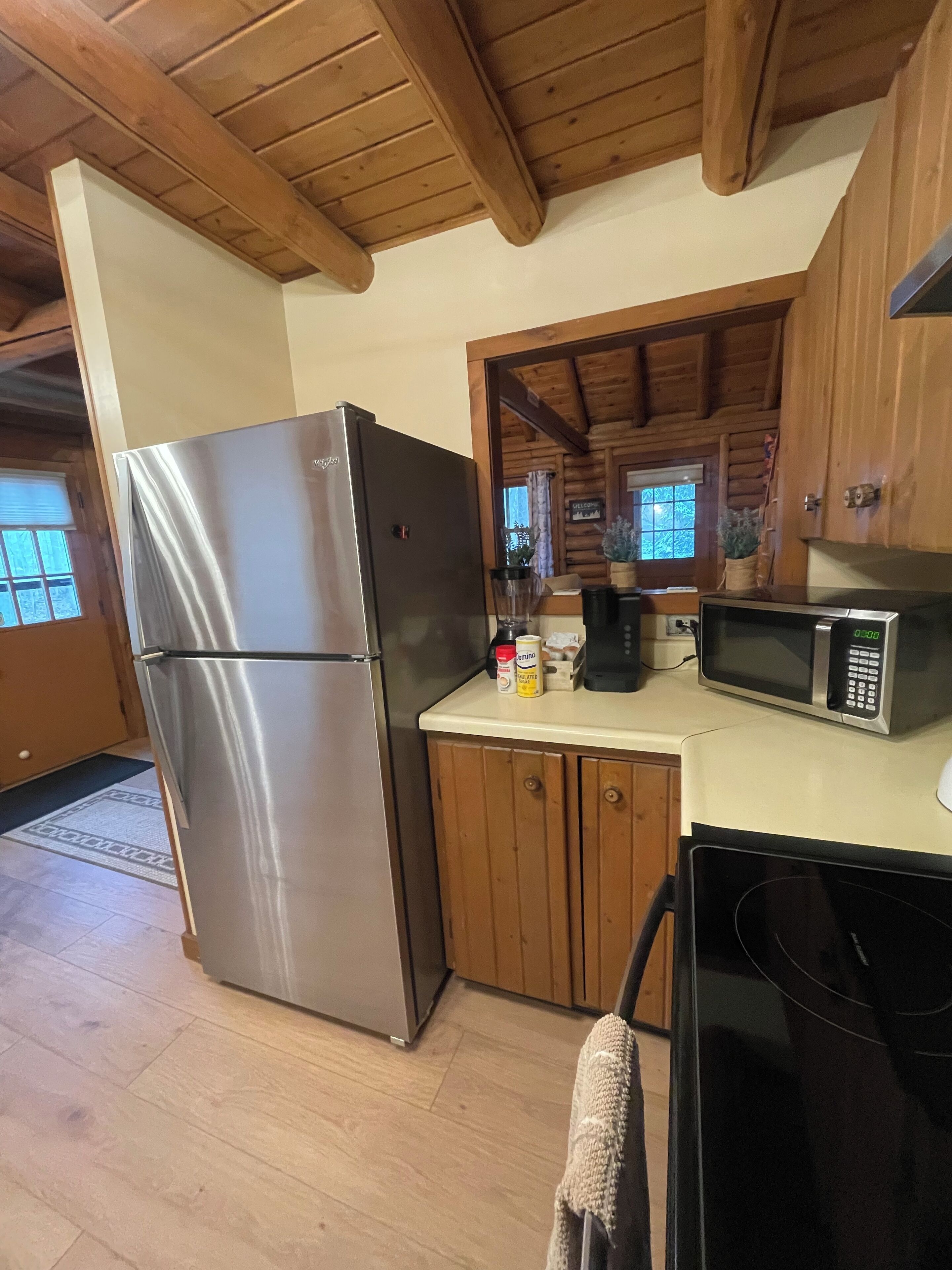 Una cocina con refrigerador de acero inoxidable, armarios de madera, microondas y techo de madera.
