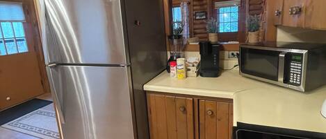 Una cocina con refrigerador de acero inoxidable, armarios de madera, microondas y techo de madera.
