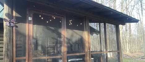 Puinen mökki, jossa on suuri ikkunallinen kuisti, penkki ja pieni puutarha-alue.