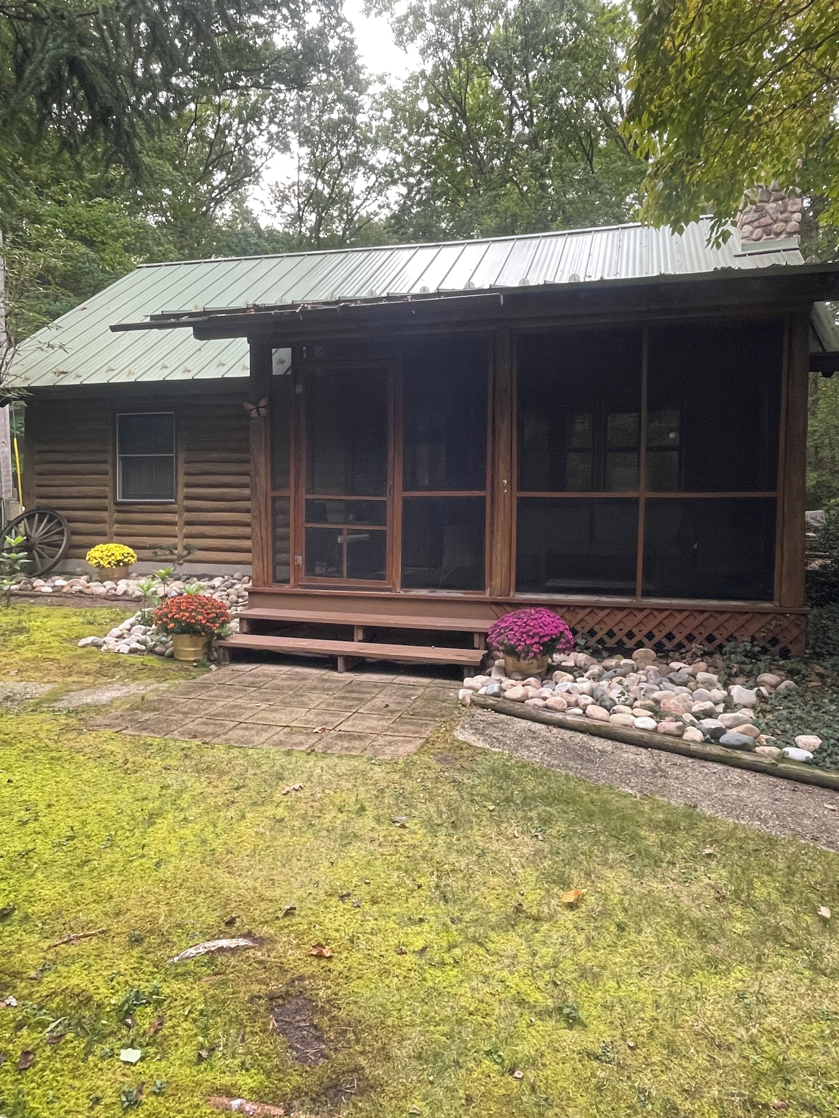 A rustic cabin with a porch, large windows, and a stone foundation.