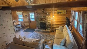 Interior acogedor de una cabaña de madera con chimenea, dos sofás, un comedor y una araña.