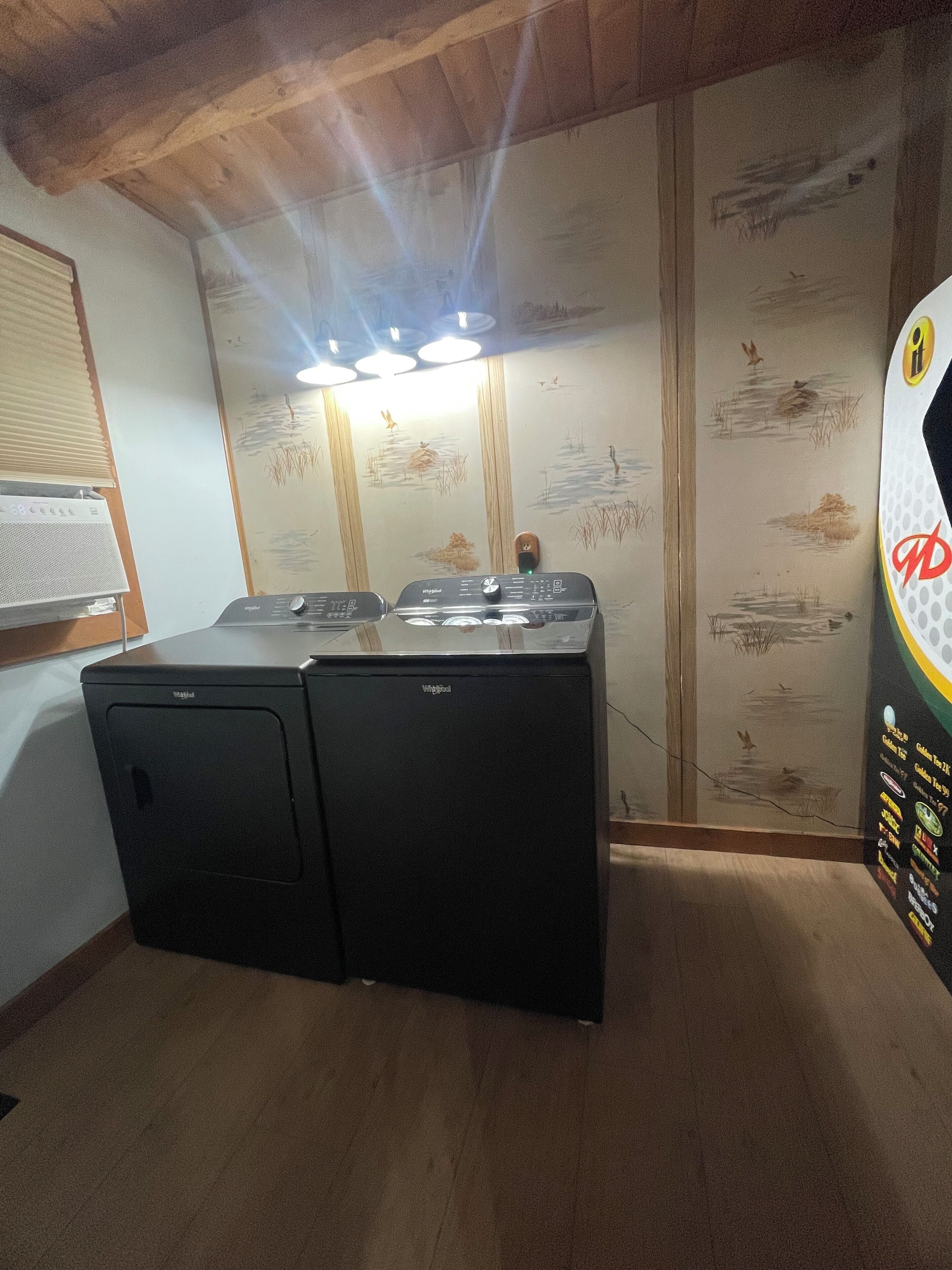 A laundry room with two Whirlpool washers, wooden ceiling beams, and a wall with a nature-themed mural.