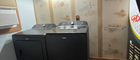A laundry room with two Whirlpool washers, wooden ceiling beams, and a wall with a nature-themed mural.