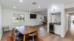 A spacious dining area with a wooden table and chairs, a kitchen with white cabinets, and large windows offering views of the outdoors. - Beautiful Furnished Arcadia Home with Camelback View Off Exeter (Phoenix)