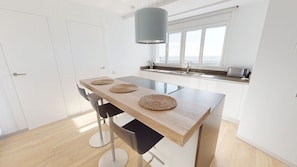 A modern kitchen with a wooden table, two chairs, a hanging light fixture, a window with a view, and a built-in oven.