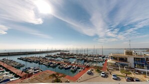 A marina with numerous boats docked, a pier extending into the water, and a building with a glass facade. - APTO PANORAMIC (Ampolla)