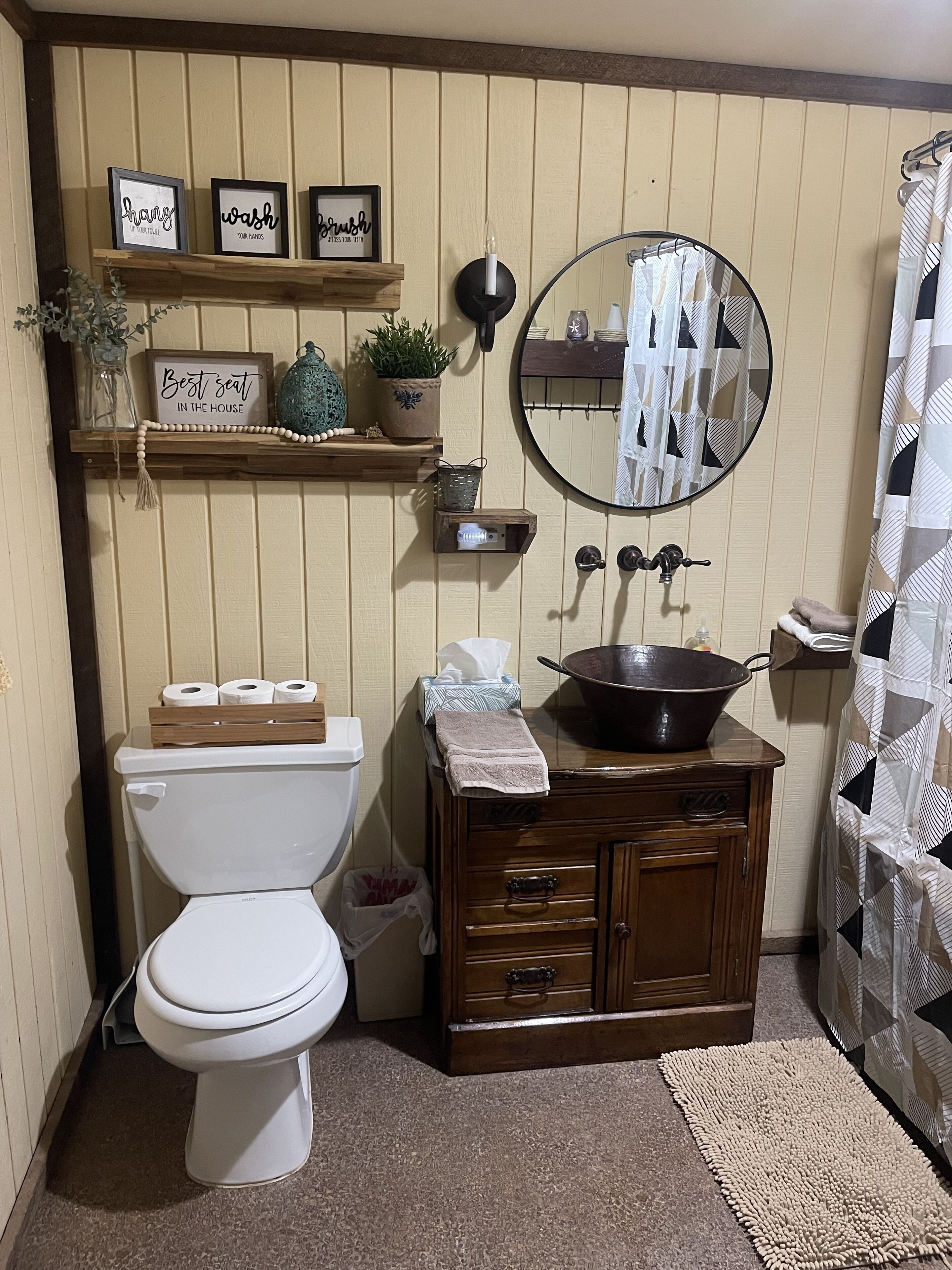 Une salle de bain comprenant des toilettes, un lavabo avec un miroir, une étagère avec des panneaux encadrés et un rideau de douche.