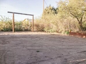 Un espacio al aire libre con suelo de tierra, una estructura de madera y follaje denso.