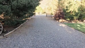 A gravel driveway leading to a wooden gate, surrounded by evergreen trees and a grassy area. - Secluded, Cozy Cabin Getaway (Monroe)
