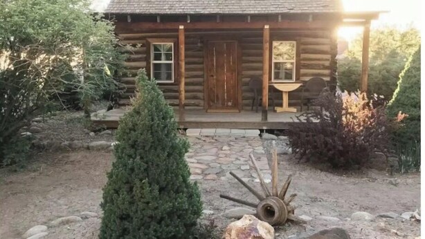 A rustic log cabin with a porch, a small table, and chairs. - Secluded, Cozy Cabin Getaway (Monroe)