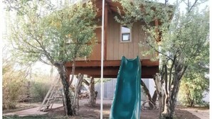 A treehouse with a slide, surrounded by trees and a wooden deck. - Secluded, Cozy Cabin Getaway (Monroe)