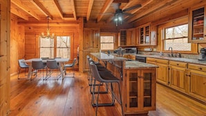 A wooden cabin interior with a dining area, kitchen, and bar stools. - Chilhowee-Big log cabin with hot tub by the Ocoee (Benton)