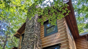 A log cabin with a stone chimney, wooden siding, and a porch. - Chilhowee-Big log cabin with hot tub by the Ocoee (Benton)
