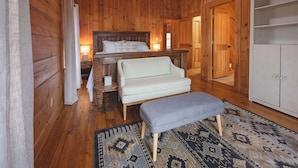 A wooden cabin bedroom with a bed, a sofa, an ottoman, a nightstand, and a wardrobe. - Chilhowee-Big log cabin with hot tub by the Ocoee (Benton)