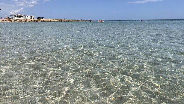 A beachfront property with clear shallow waters, a sandy beach, and a distant house. - Apartment San Lorenzo in Villa (San Lorenzo)