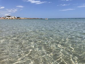 A beachfront property with clear shallow waters, a sandy beach, and a distant house. - San Lorenzo Apartment in Villa (San Lorenzo)
