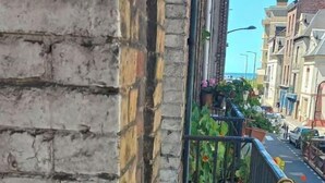 A balcony with a wooden chair and a table, overlooking a street with buildings and a clear sky. - Loft en Duplex Avec vue sur Plage et Chenal (Dieppe)