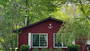 Ein rotes Holzgebäude mit einem weißen Ankersymbol, umgeben von üppigen, grünen Bäumen und Gras.