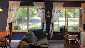 Ein Wohnzimmer mit einer Couch, einem Esstisch und zwei mit Anker-Motiven versehenen Fenstern.