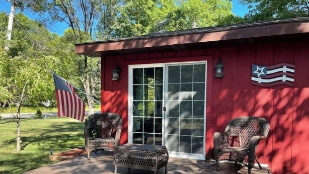 Ein rotes Gebäude mit einer Veranda und zwei Korbstühlen, eine amerikanische Flagge ist ebenfalls zu sehen.