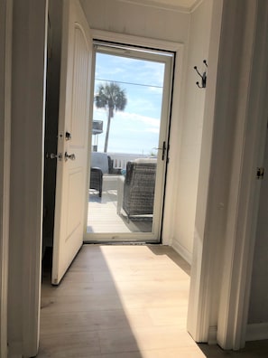 A hallway leading to a balcony with a view of the beach and palm trees. - Pet Friendly - Ocean View Huge Deck -  Across from Beach - Walk to Center St (Folly Beach)