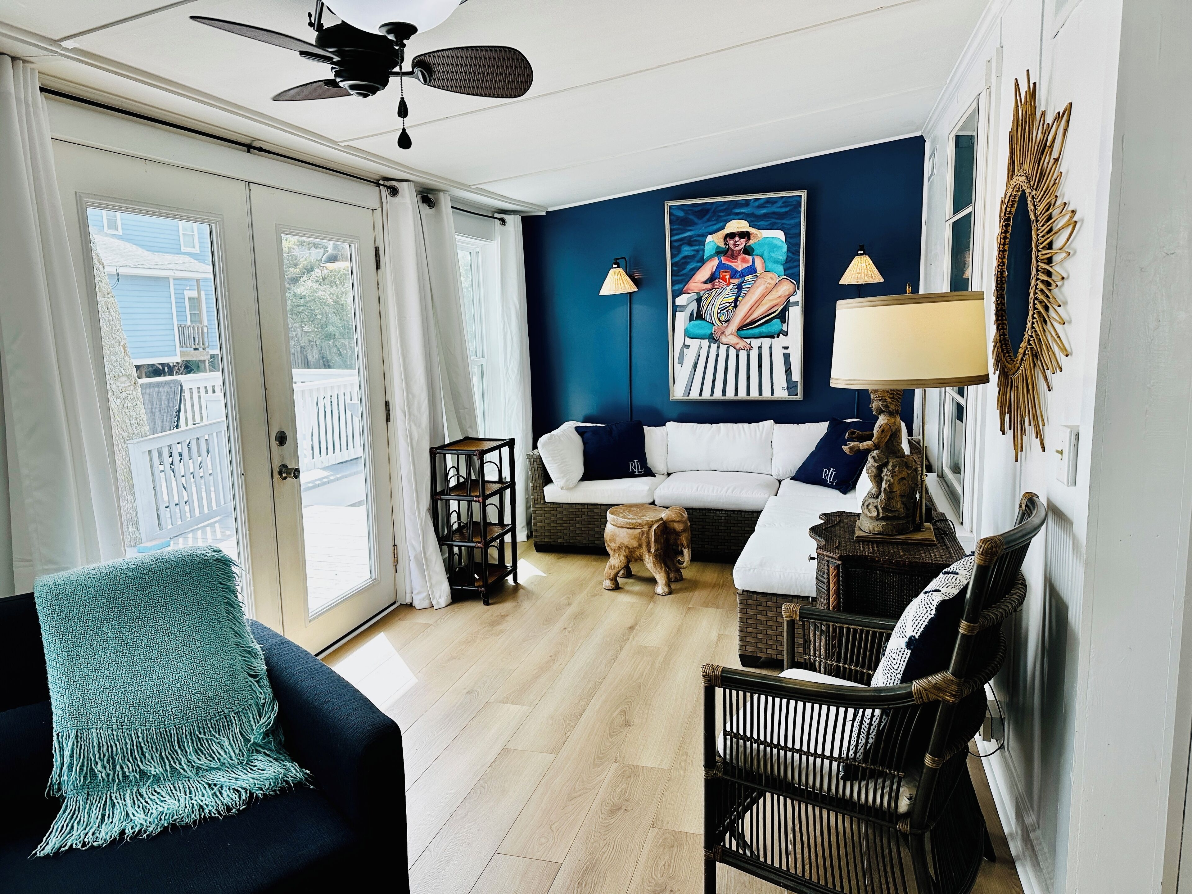 Un salon avec un canapé blanc, un fauteuil noir, un petit chien et un ventilateur de plafond.