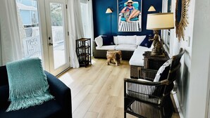 A living room with a white sofa, a black chair, a small dog, and a ceiling fan. - Pet Friendly - Ocean View Huge Deck -  Across from Beach - Walk to Center St (Folly Beach)