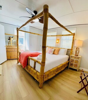 Une chambre avec un lit à baldaquin, un plancher en bois et une petite commode en bois.