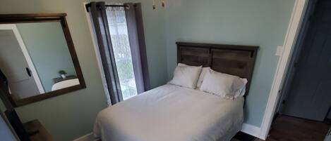 Un dormitorio con cama, ventilador de techo, espejo y ventana con cortinas.