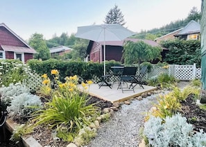 Una terrazza giardino con tavolo e sedie, circondata da diverse piante e un recinto bianco.