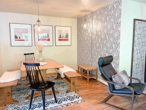 Un espace repas comprenant une table en bois, des chaises, un banc et un tapis à motifs.