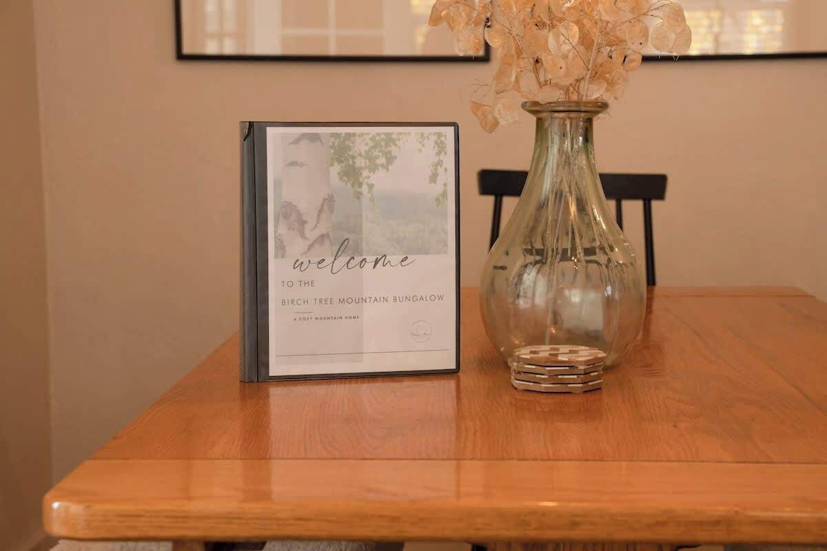A welcome sign and a vase with dried flowers on a wooden table.